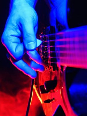 Rock concert. Guitarist plays the guitar. The guitar illuminated with bright neon lights. Focus on hands. No face shown