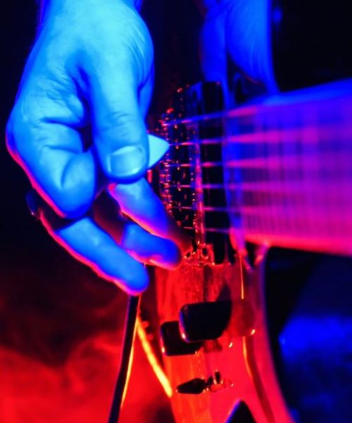 Rock concert. Guitarist plays the guitar. The guitar illuminated with bright neon lights. Focus on hands. No face shown